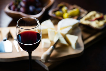 Pouring red wine into the glass above the table set with grape cheese appetizers