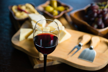 Pouring red wine into the glass above the table set with grape cheese appetizers