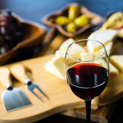 Pouring red wine into the glass above the table set with grape cheese appetizers