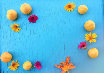 Summer fresh apricots on a wooden turquoise table close-up with bright summer flowers. Horizontal view from above. Copy space