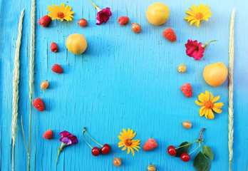 Fresh fruits and berries, apricots, gooseberries and raspberry on a wooden turquoise table close-up with bright summer flowers. Sun light Horizontal view from above. Copy space