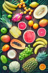 Wall murals Fruits Assortment of tropical fruits with leaves of palm trees and exotic plants on dark wooden background