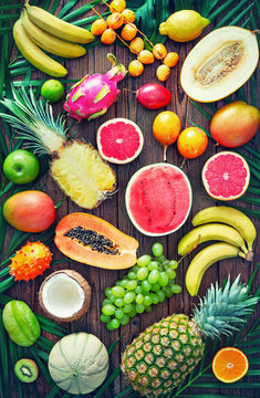 Assortment of tropical fruits with leaves of palm trees and exotic plants on dark wooden background