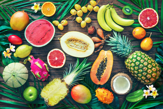 Fototapeta Assortment of tropical fruits with leaves of palm trees and exotic plants on dark wooden background