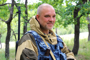 On the hunt. A man of 35-40 years old, a military hunter with a smile on his face stands with a firearm in the forest.