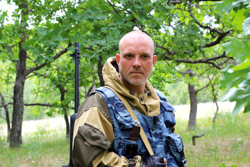 Fototapeta premium Hunting season. A man of 35-40 years old, a military hunter with a serious face is standing with a firearm in the forest.