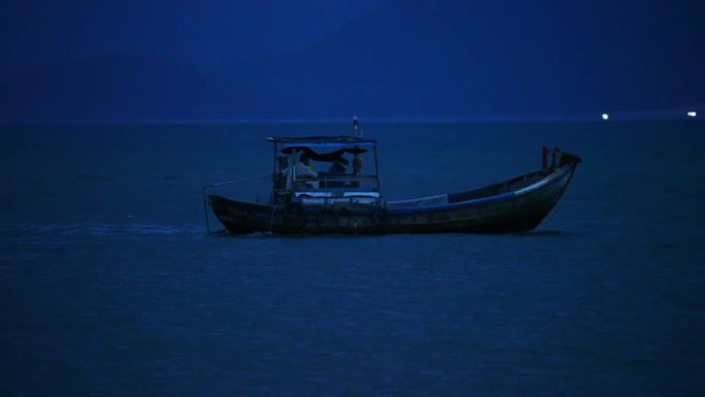 Fisherman in a small wooden fishing boat navigating across the south china sea, night fishing high definition stock footage clip.
