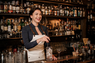 Smiling female bartender stirring an ice in the glass