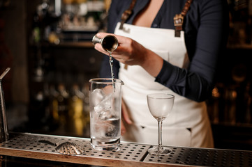 Female bartender adding an alcohol into the glass with ice