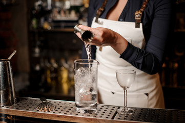 Bartender girl adding an alcohol into the glass with ice