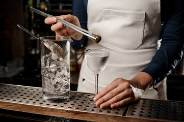 Bartender girl adding to the cocktail one olive with tweezers