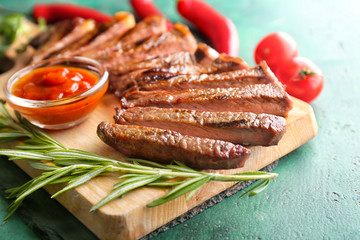 Board with tasty cut steak, rosemary and sauce on green background