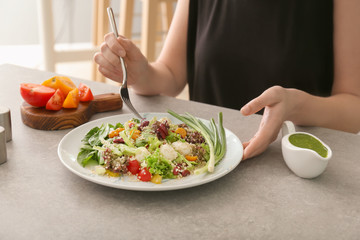 Woman eating tasty quinoa salad at table