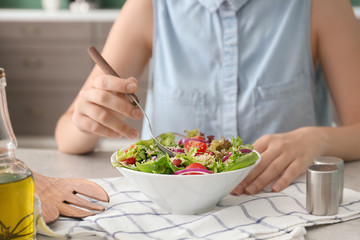 Obraz na płótnie Canvas Woman eating tasty quinoa salad at table