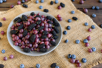 Fresh berries of blueberry, blackberry and gooseberry on a plate. It can be used as a background