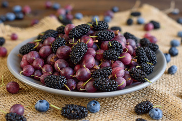 Fresh berries of blueberry, blackberry and gooseberry on a plate. It can be used as a background