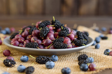 Fresh berries of blueberry, blackberry and gooseberry on a plate. It can be used as a background