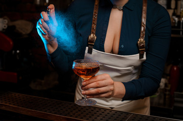 Female bartender spraying on the orange cocktail in her hand