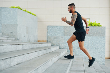Fototapeta na wymiar Side view of man in black sportswear running up stairs while working out outdoors on street looking focused