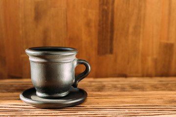 Black clay mug with coffee on a white background. a clay cup of black color on a wooden table. side view