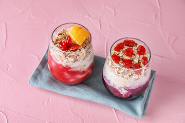 Tasty oatmeal desserts in glasses on color textured background