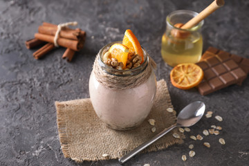 Tasty oatmeal dessert with sliced orange and walnuts in glass jar on grey background