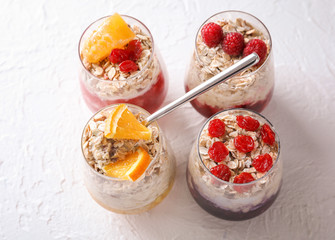 Tasty oatmeal desserts with fresh orange and berries in glasses on light textured background