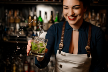 Smiling bartender girl holding an fresh cocktail with lime and mint