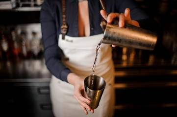 Bartender girl pourring an alcoholic drink from one steel cup to another