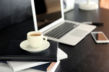 Workplace with cup of coffee, notebooks and laptop on table in office