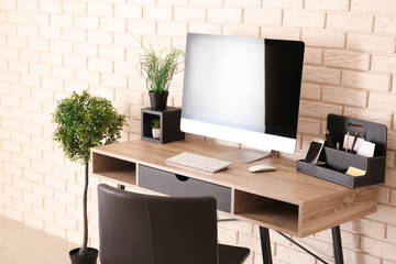 Stylish workplace with computer on table near brick wall in office