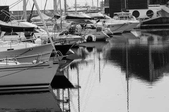 Luxury yachts moored in marina. Boats reflected in the water of Deauville harbor, France. Close up. Yachting, vacation, luxury lifestyle and wealth concept. Black and white