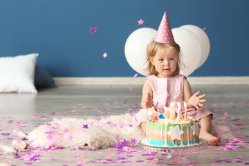 Cute little girl with birthday cake sitting on fluffy rug indoors