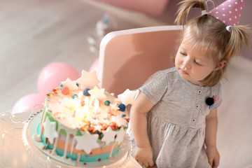 Cute little girl with birthday cake sitting on chair in room