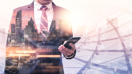 The double exposure image of the businessman using a smartphone during sunrise overlay with cityscape image. The concept of modern life, business, city life and internet of things.