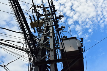 Large steel eletric support with a lot of tangled wires, cables. On the pole there is a step-down...