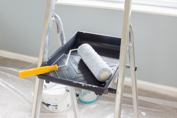 Painting and decorating with a roller and tray on a set of metal step ladders with cans of paint...