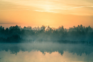 Obraz na płótnie Canvas A beautiful, colorful landscape of a misty swamp during the sunrise. Atmospheric, tranquil wetland scenery with sun in Latvia, Northern Europe.