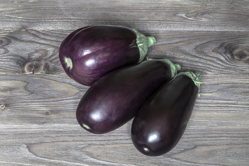 three purple eggplant on an old wooden background