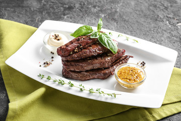 Tasty grilled meat with basil, sauces and spices on plate