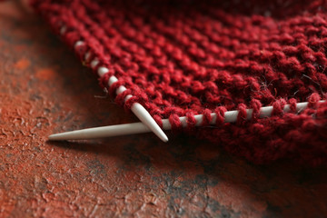 Knitting needles with unfinished clothes on table, closeup