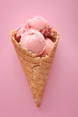 Waffle cone with delicious strawberry ice-cream on color background