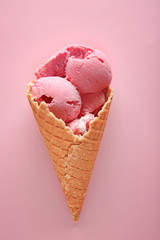 Waffle cone with delicious strawberry ice-cream on color background