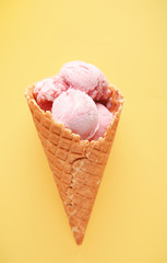 Waffle cone with delicious strawberry ice-cream on color background