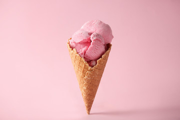 Waffle cone with delicious strawberry ice-cream on color background
