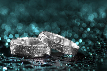 Wedding rings with water drops on cyan background with copy space.