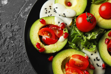 Plate with ripe avocado, tomatoes and herbs on dark background, closeup