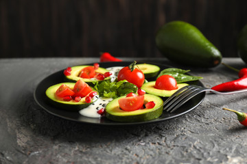 Plate with ripe avocado, tomatoes and herbs on dark table