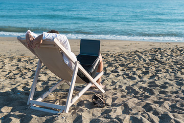 Young woman in office clothes with a laptop on the beach on a background of the sea in a summer sunny day. Concept