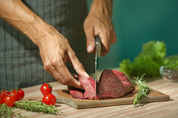 Man cutting raw meat on board in kitchen